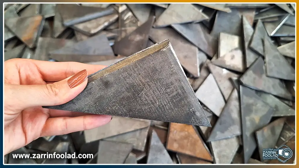 اپراتور، لچکی فولادی برشخوردهای را برای بررسی در دست دارد و در کنار دپوی لچکیهای آهنی تولیدشده ایستاده است.